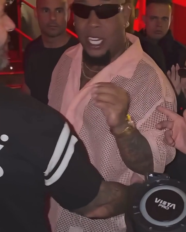 Bulin 47 AI clip opening: a fan holds a portable speaker up to a man in sunglasses and a pink mesh shirt in a red-lit club entrance