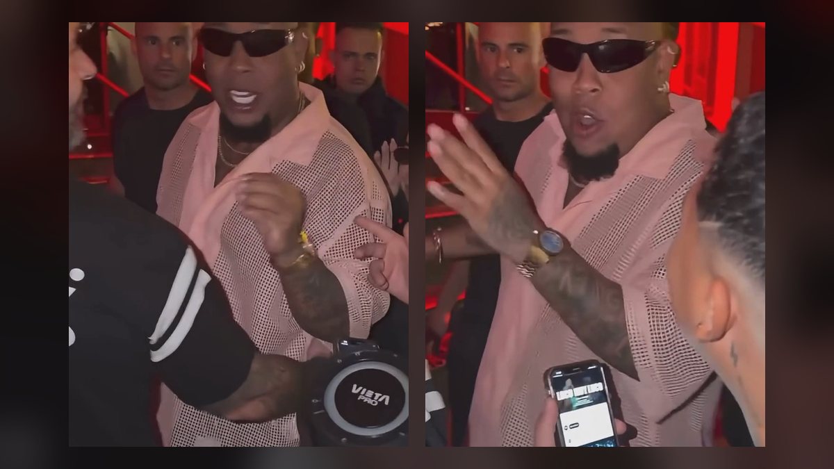 Bulin 47 in black sunglasses and a pink mesh shirt freestyles at a red-lit entrance while a fan holds a speaker